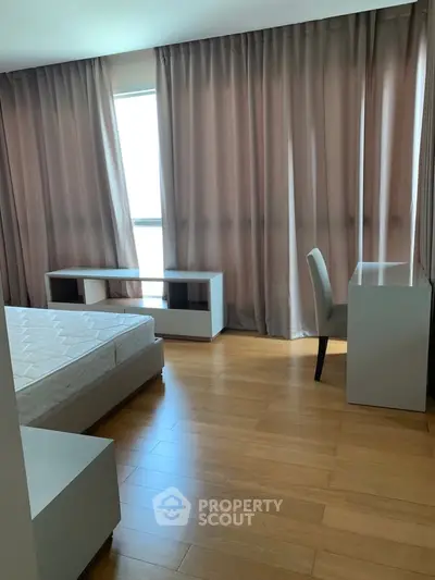 Spacious bedroom with wooden flooring and ample natural light from large windows.