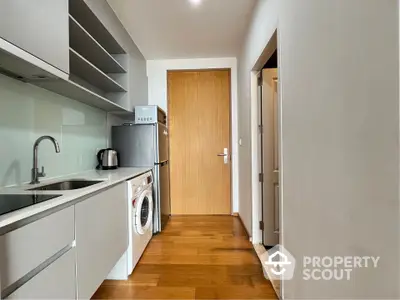 Modern kitchen with sleek cabinetry, washing machine, and compact fridge in a cozy apartment setting.