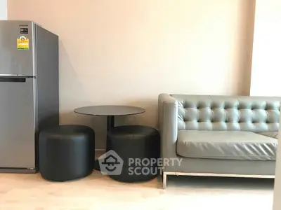 Modern living room with sleek gray sofa, compact dining table, and stainless steel fridge.