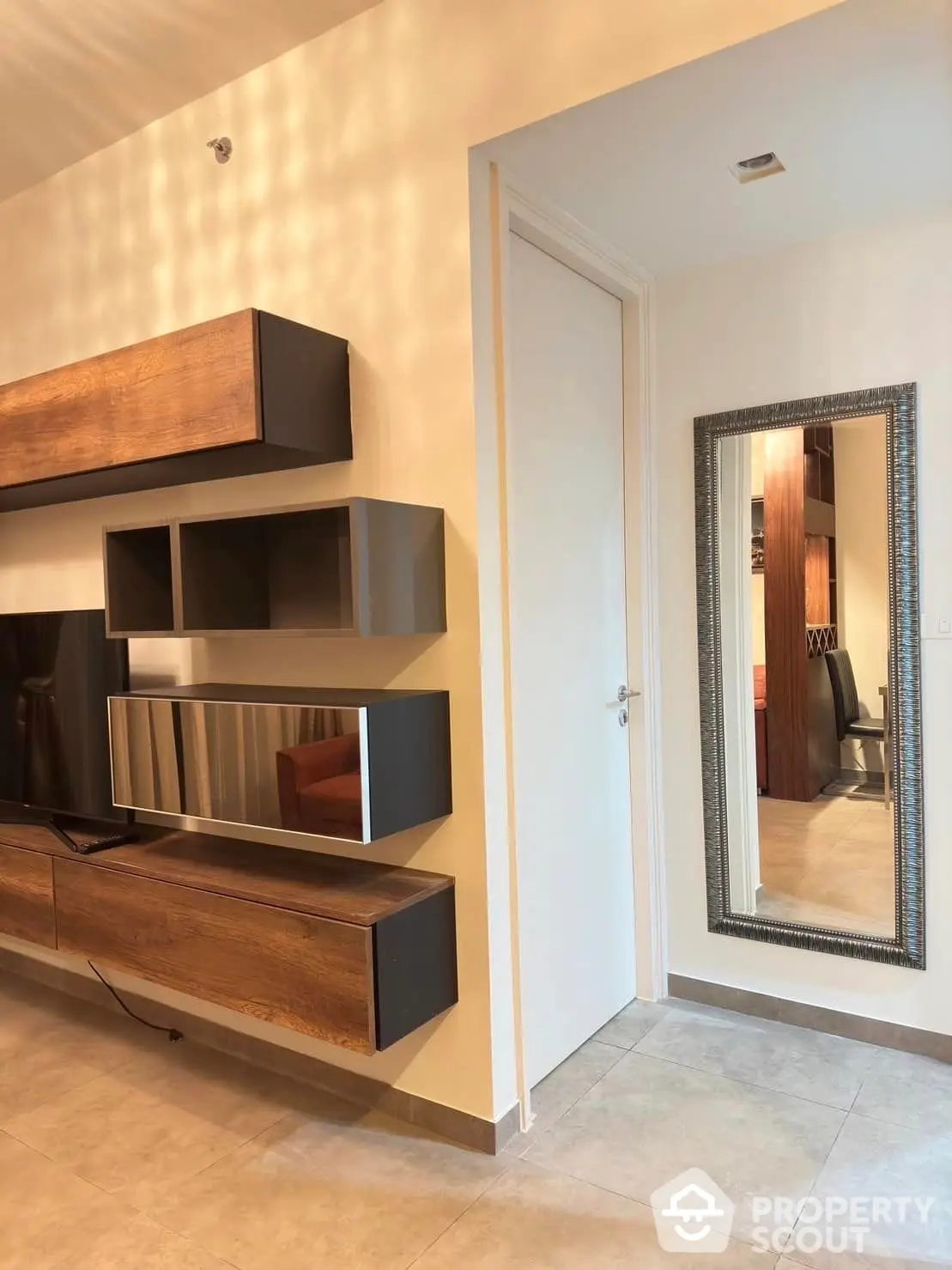 Modern living space featuring sleek wooden entertainment unit with ample shelving, complemented by elegant tiled flooring and a chic framed mirror, creating a warm and inviting atmosphere.