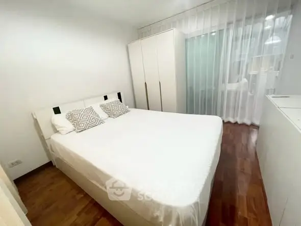 Cozy bedroom with wooden flooring and white decor, featuring a comfortable bed and wardrobe.