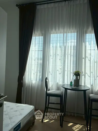 Cozy bedroom with natural light, elegant curtains, and a small dining table set.