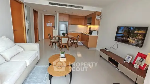 Modern open-plan living room with kitchen, featuring sleek furniture and a wall-mounted TV.