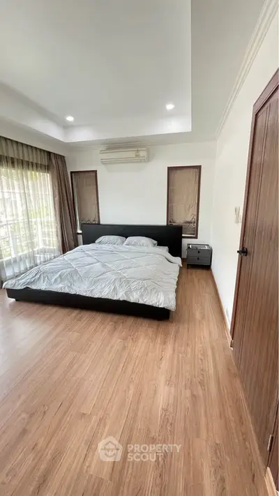 Spacious bedroom with wooden flooring and large windows for natural light.