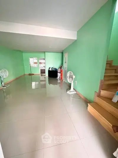 Spacious interior with glossy tiled floors and vibrant green walls, featuring a staircase and fans for ventilation.