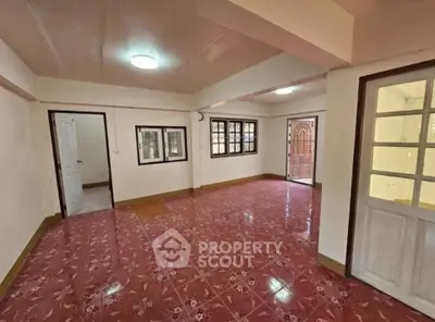 Spacious living room with red tiled flooring and ample natural light.