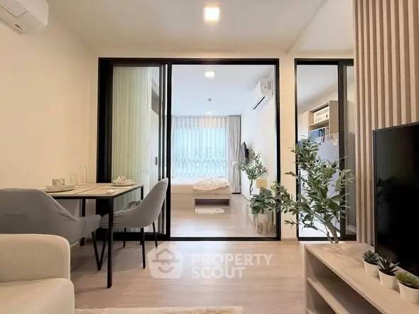 Modern open-plan living room with dining area and bedroom, featuring sleek furniture and natural light.