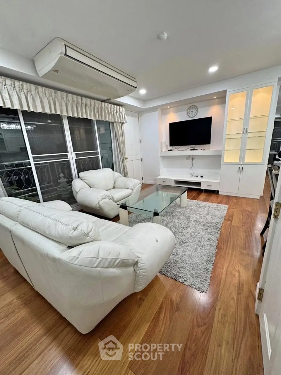 Spacious living room with elegant white furniture and modern decor, featuring a large window for natural light.