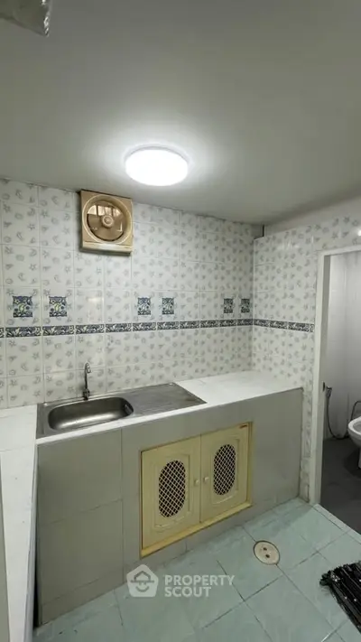 Compact bathroom with tiled walls and sink, featuring a small ventilation fan.