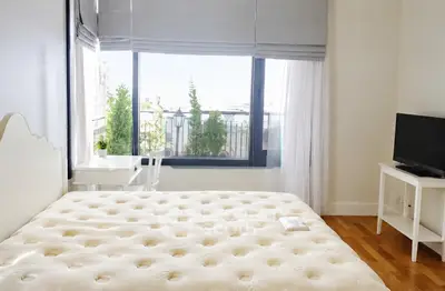 Bright bedroom with large window and city view, featuring a cozy bed and modern decor.