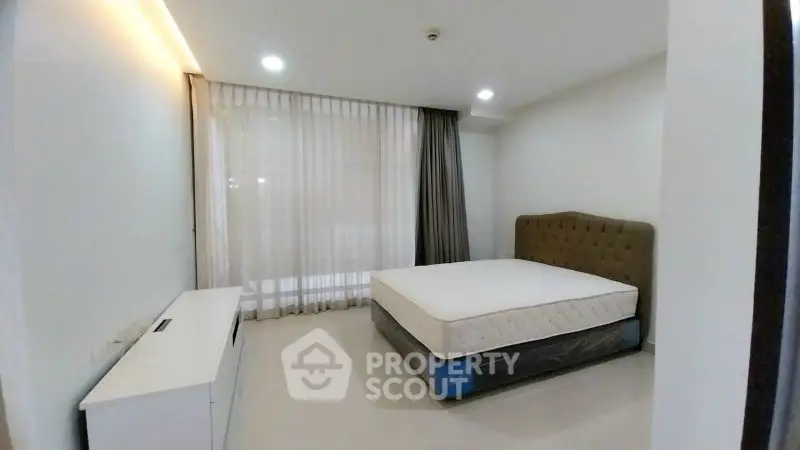 Spacious bedroom with large window and modern furnishings in a stylish apartment.