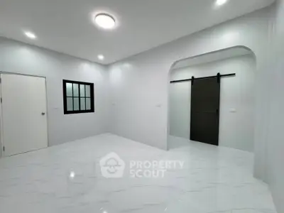 Spacious modern room with sleek white flooring and sliding barn door, perfect for versatile living space.