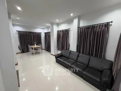 Spacious living room with elegant black sofa and dining area, featuring modern design and ample natural light.