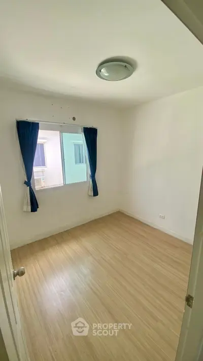 Spacious empty bedroom with wooden flooring and natural light from window.