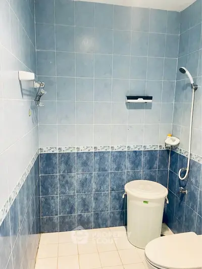 Modern blue-tiled bathroom with shower and storage bin, perfect for compact living spaces.