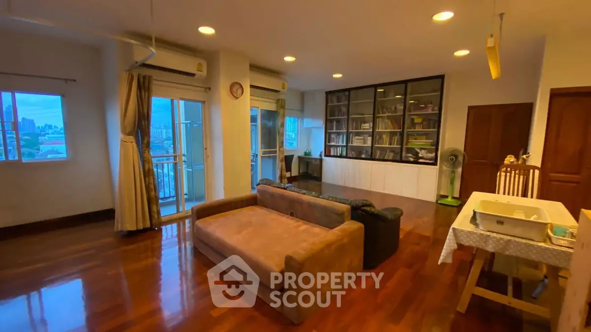 Spacious living room with wooden flooring and large windows offering city views.