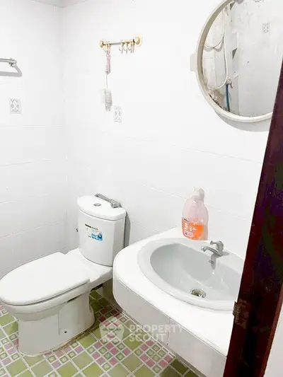 Compact bathroom with white tiles, round mirror, and essential fixtures.