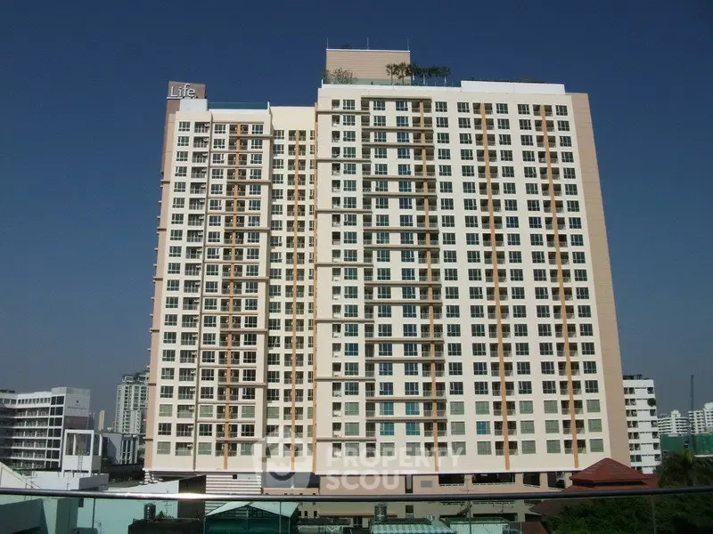 Modern high-rise apartment building with clear blue sky backdrop, showcasing urban living at its finest.