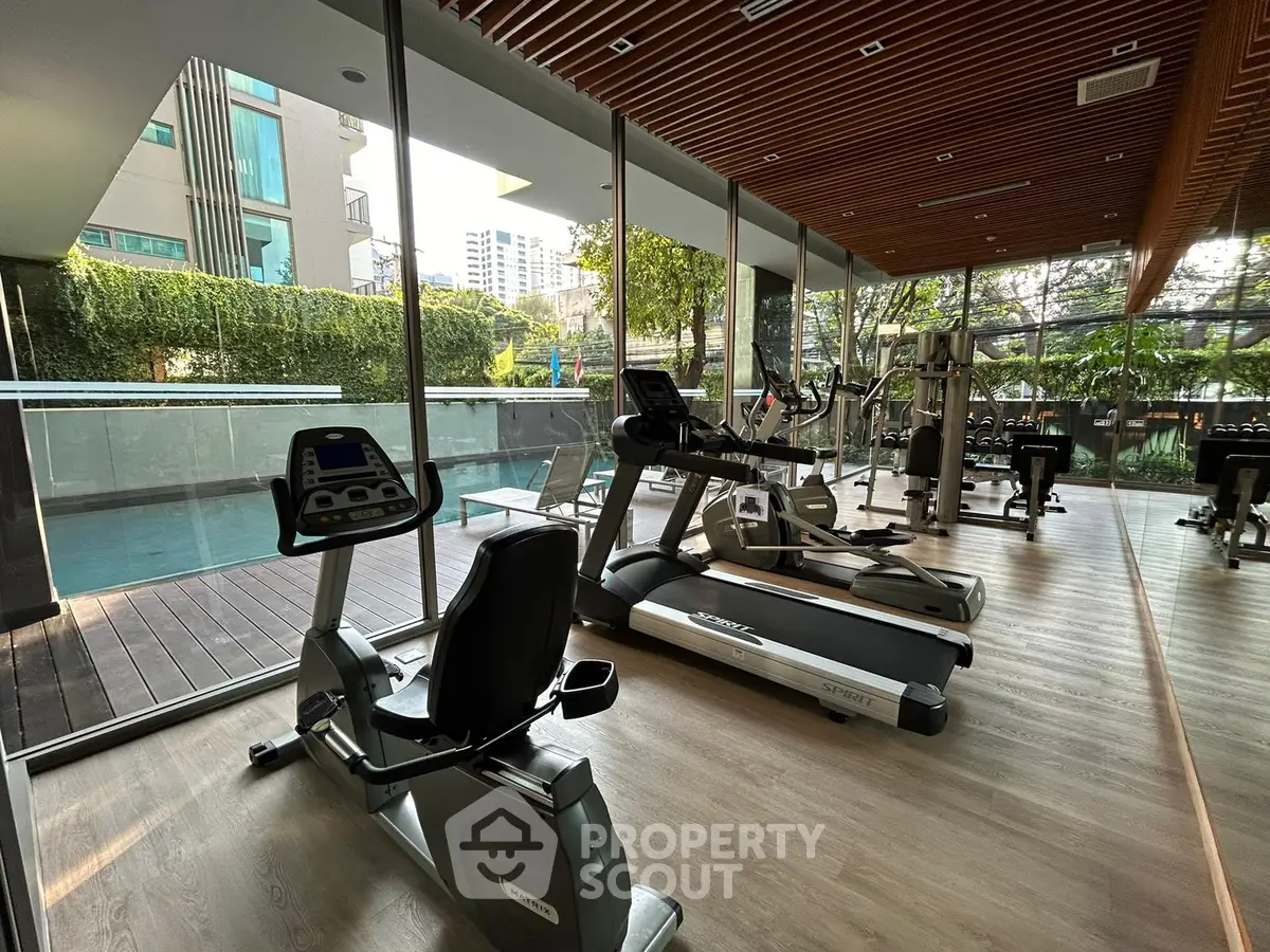Modern gym with exercise equipment and pool view in luxury apartment complex.