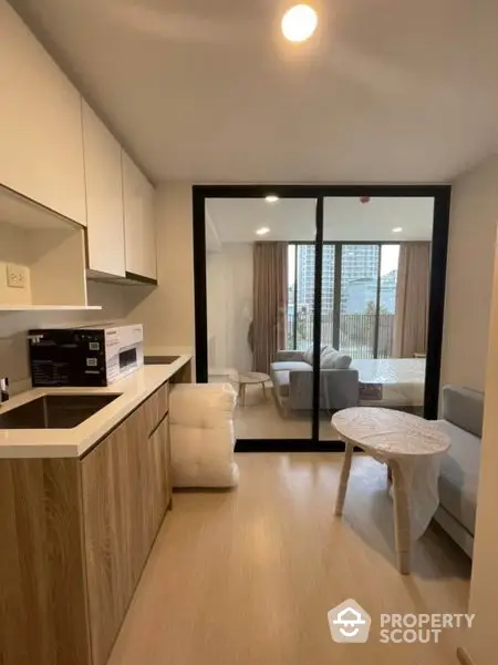 Modern apartment with open layout kitchen featuring built-in oven and sleek cabinetry, leading to a cozy living area with natural light.