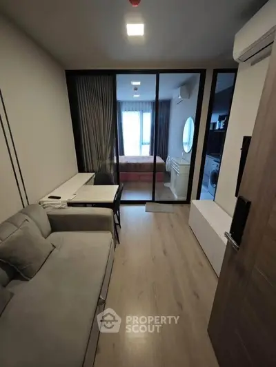 Modern living room with sleek design and glass partition leading to bedroom, featuring cozy sofa and stylish decor.