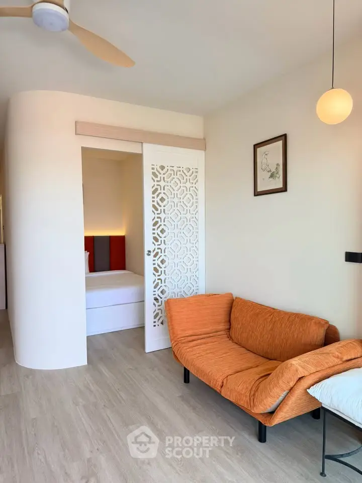 Modern living room with stylish orange sofa and decorative sliding door leading to bedroom.