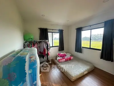 Cozy bedroom with large windows and scenic views, featuring a minimalist setup with a mattress and clothing rack.