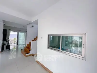 Modern interior with sleek staircase and large window, bright and airy living space.