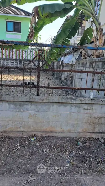 Vacant land plot with boundary wall and banana trees, ideal for development in a residential area.