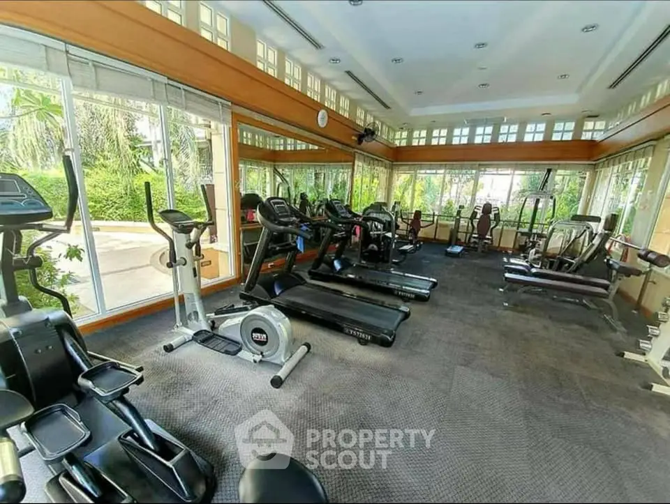 Spacious gym with modern equipment and large windows offering a garden view.