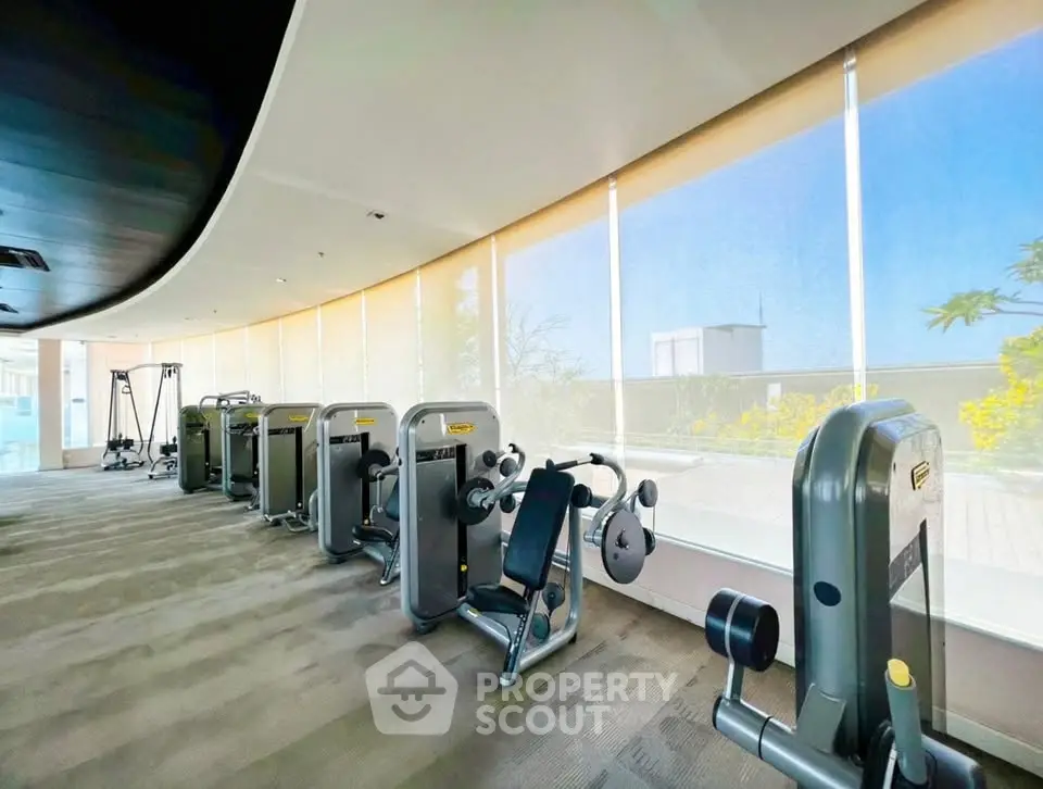 Spacious modern gym with state-of-the-art equipment and panoramic windows offering a scenic view.