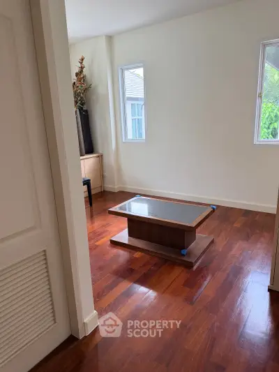 Spacious room with hardwood floors and modern coffee table, featuring natural light from large windows.