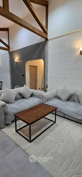 Spacious living room with modern decor and cozy seating area, featuring exposed beams and stylish lighting.