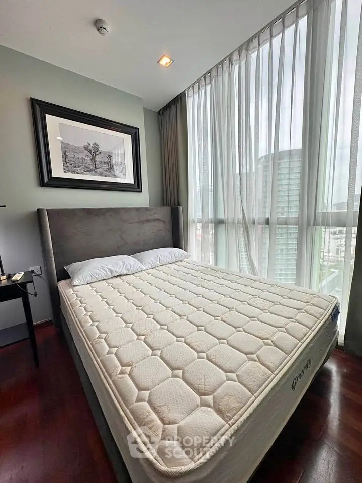Modern bedroom with large windows and city view, featuring a comfortable bed and stylish decor.