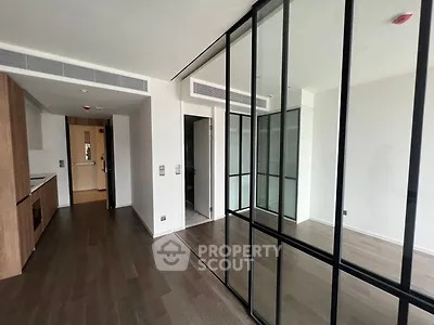 Modern apartment interior with glass partitions and wooden flooring, featuring a sleek kitchen area.