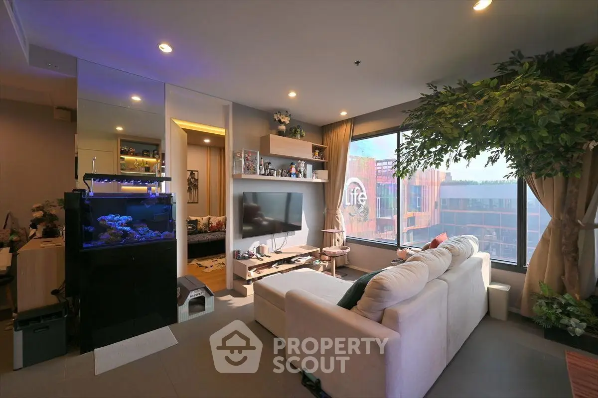 Modern living room with large window and aquarium, featuring cozy seating and stylish decor.