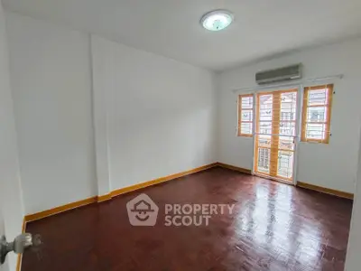 Spacious empty room with wooden flooring and large windows in a modern apartment.