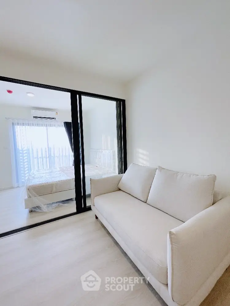 Modern apartment with cozy living room and bedroom separated by glass partition, bright and airy space.
