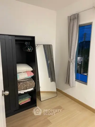 Cozy bedroom corner with wardrobe, mirror, and window view.