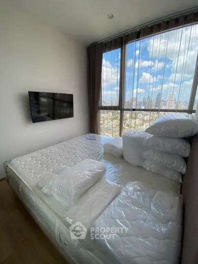 Modern bedroom with large windows offering stunning city views, featuring a wall-mounted TV and cozy bedding.