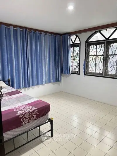 Spacious bedroom with tiled floor and large windows, featuring blue curtains and a cozy bed.