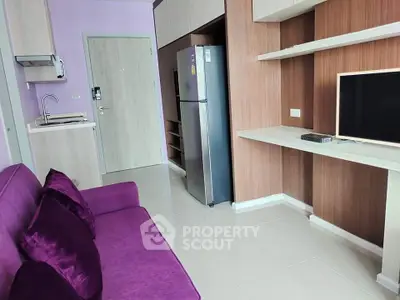 Modern living room with purple sofa, sleek TV setup, and compact kitchen area.