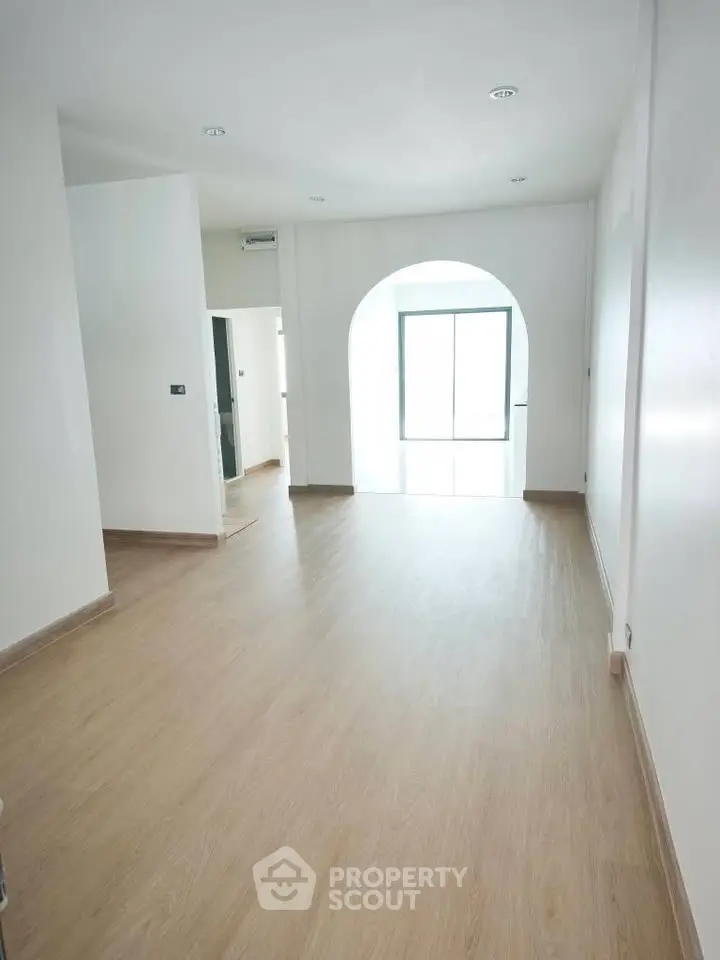 Spacious and bright interior with elegant wooden flooring and archway leading to natural light.