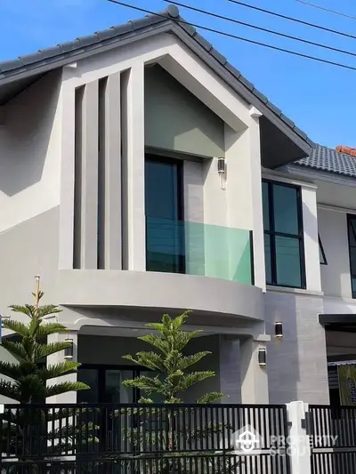 Modern two-story house with sleek design and large windows, featuring a stylish balcony and contemporary facade.