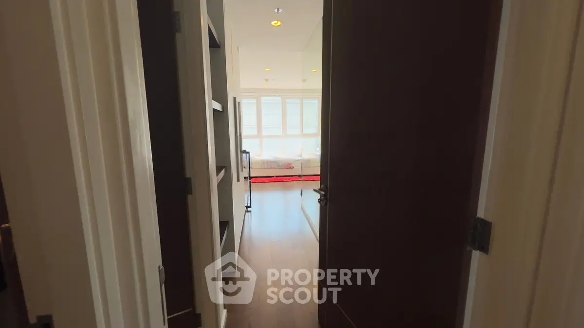 Inviting hallway leading to a bright living room with large windows and hardwood floors.