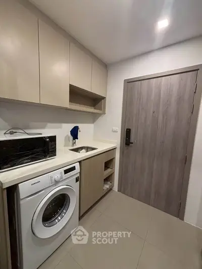 Modern compact kitchen with washing machine and microwave in sleek apartment.