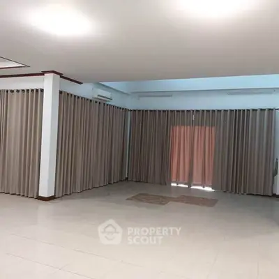 Spacious empty room with tiled floor and large windows with curtains