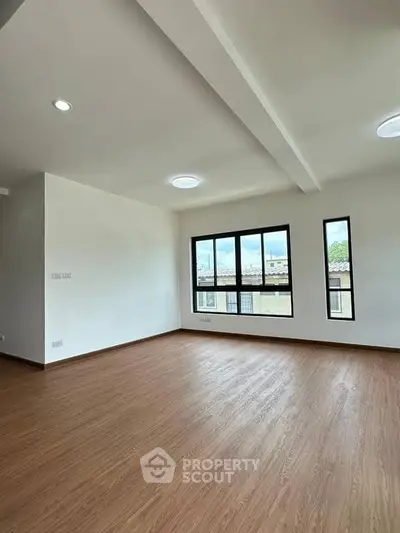 Spacious empty room with large windows and wooden flooring, perfect for customization.