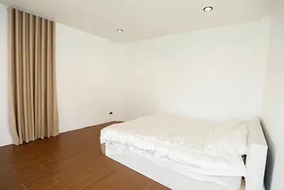 Minimalist bedroom with wooden flooring and beige curtains