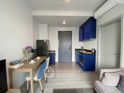 Modern apartment interior with compact kitchen and dining area, featuring sleek blue cabinets and cozy seating.
